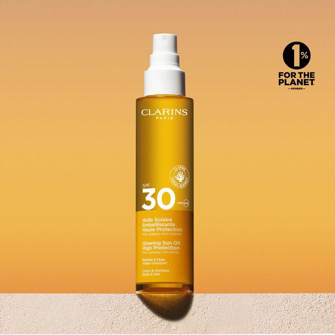 Packshot uno spray di olio solare 30 capelli e corpo con un messaggio che annuncia l’impegno Clarins a tutela dell’ambiente